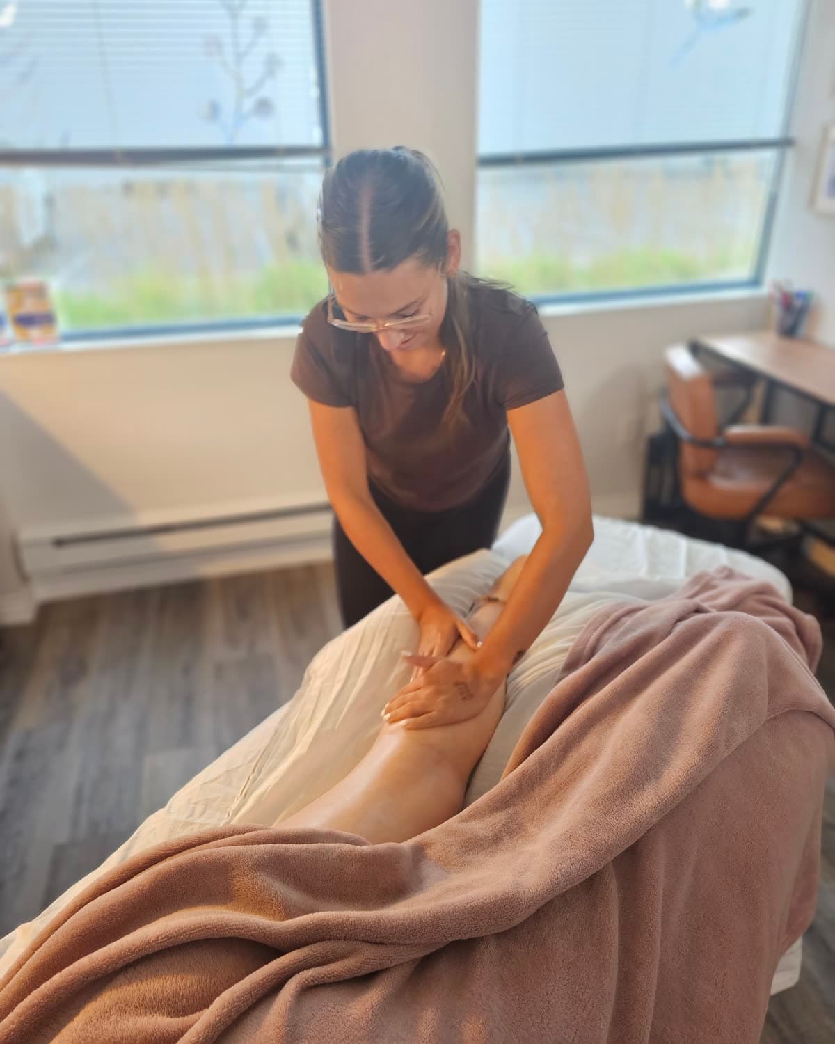A massage therapist working along a client's leg beside a bright window at Back in Health