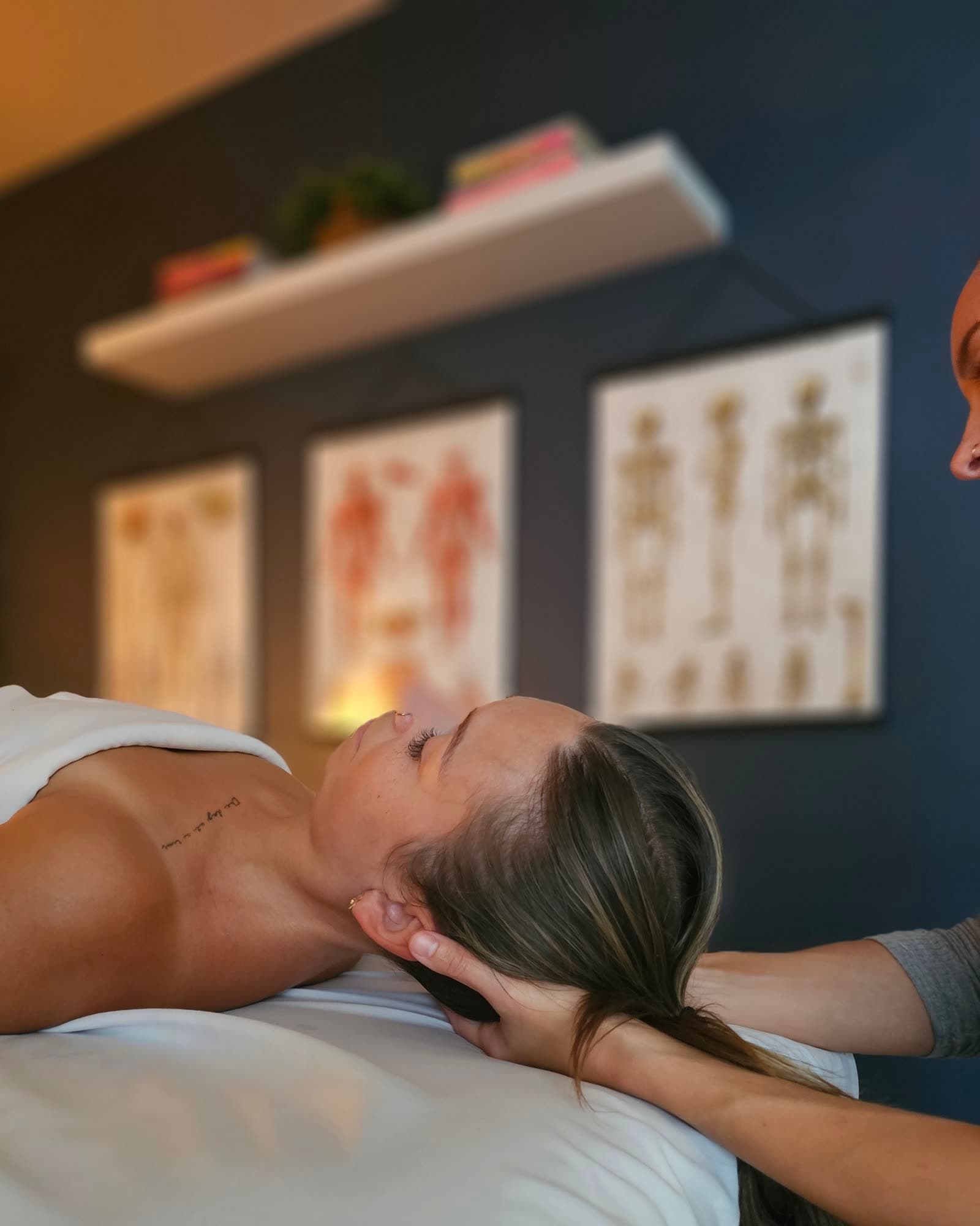 Gentle hands-on work cradling a client's head and neck beneath anatomy charts