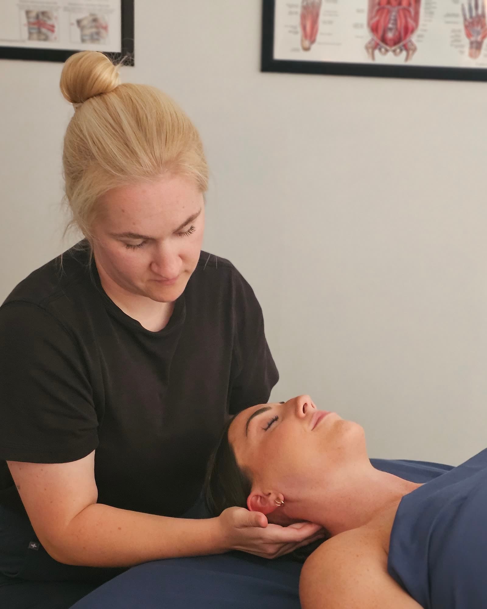 A practitioner assessing a client's neck with hands-on treatment as she lies face up on the table