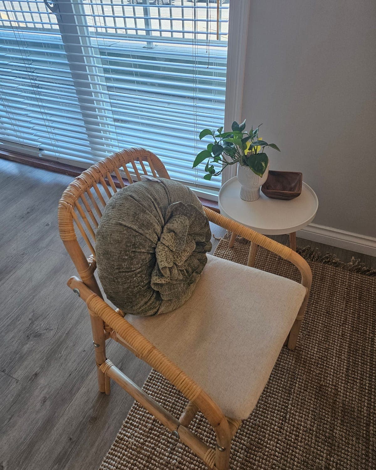 A rattan chair with a green cushion beside a window and a small plant, in a Back in Health treatment room