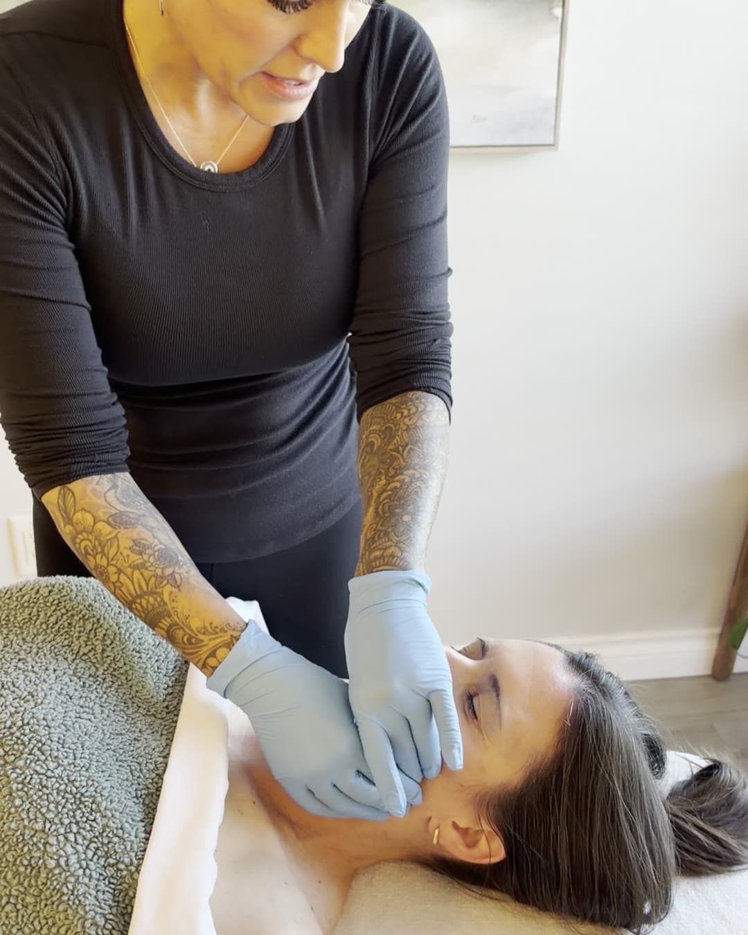 A gloved massage therapist working gently along a client's jaw